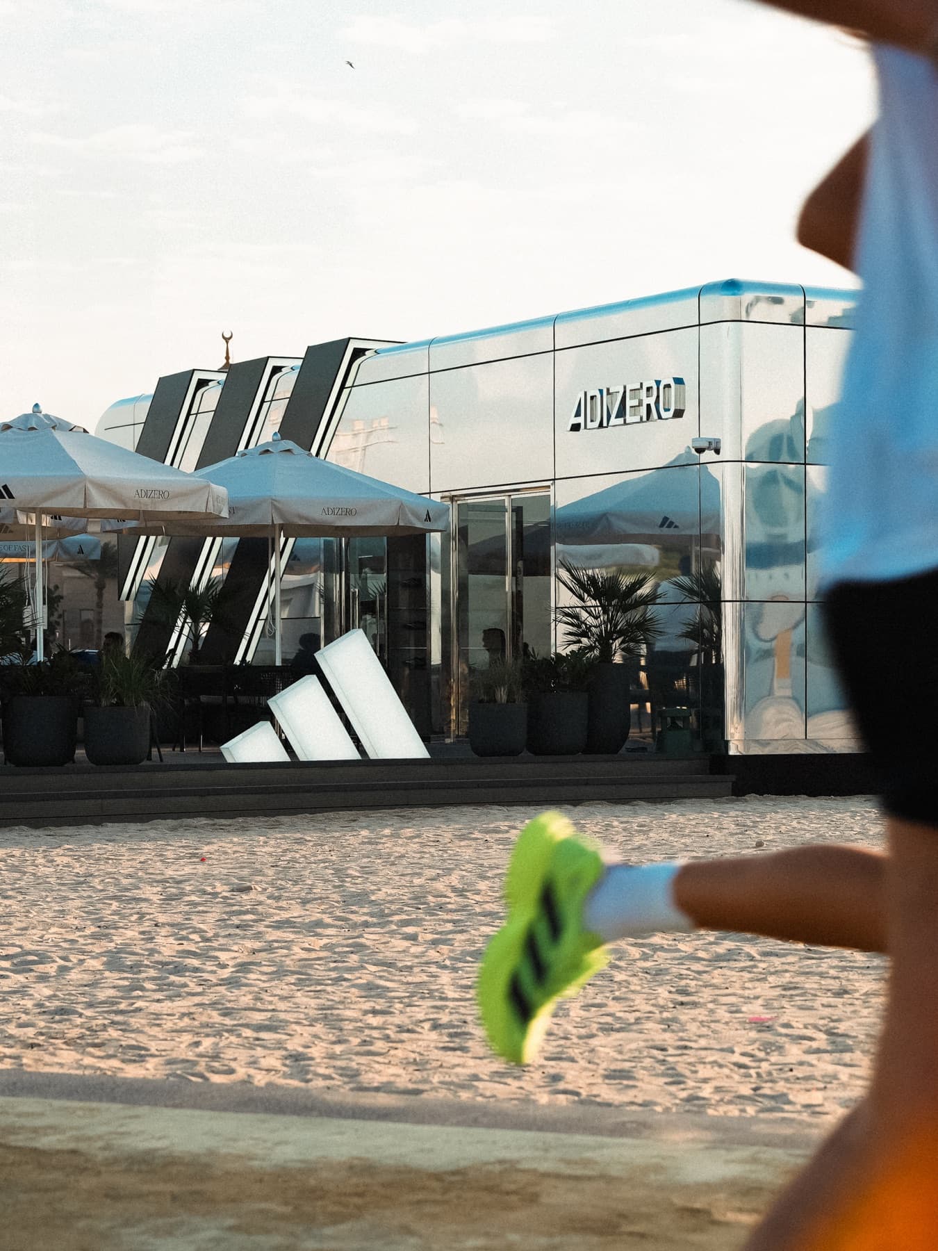 A runner in neon shoes passing the mirrored Adizero pavilion